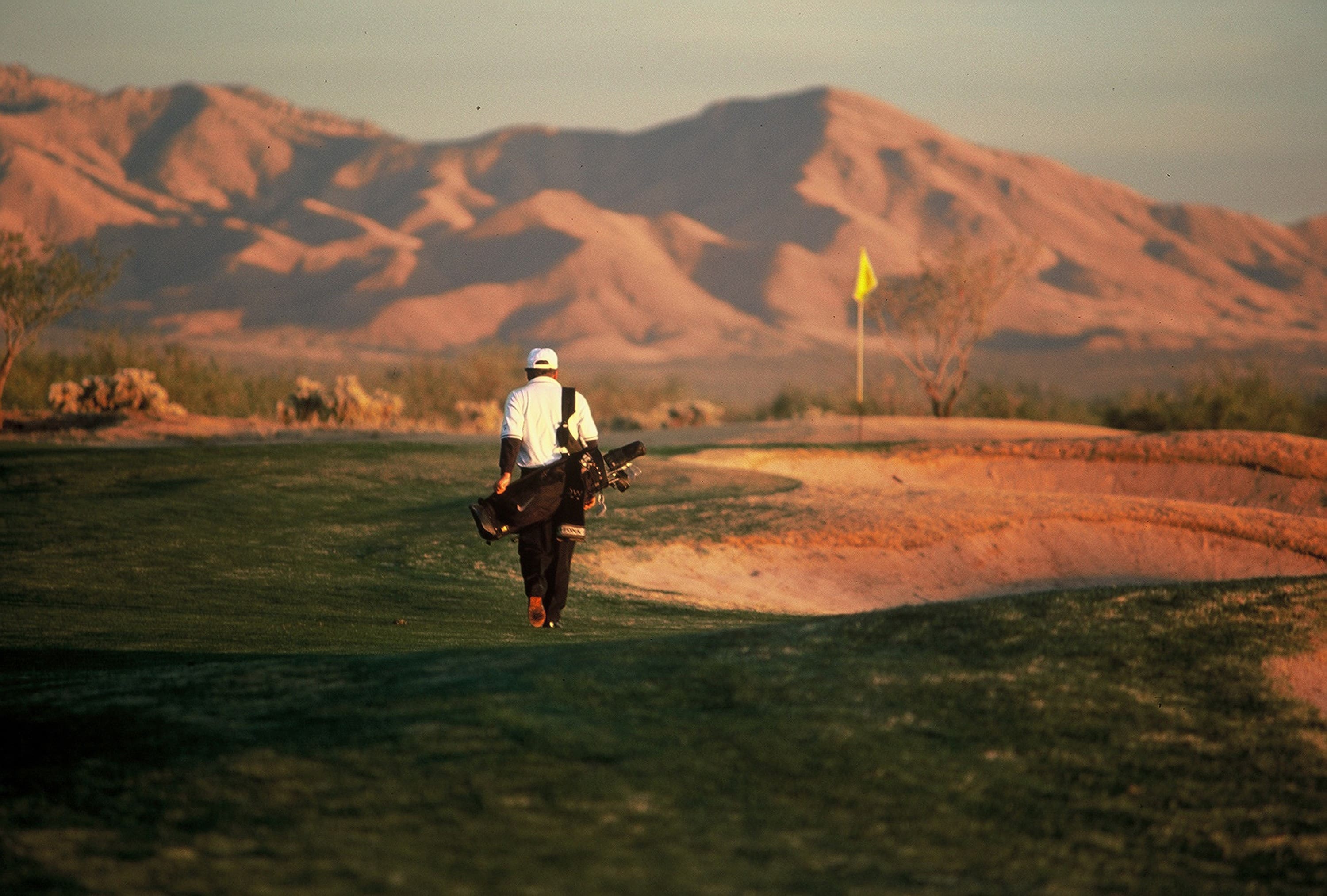 A man walking across the grass holding golf clubs.