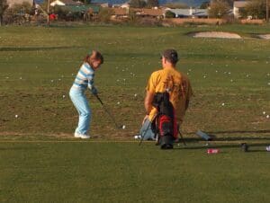 A young girl and boy playing golf on the green.