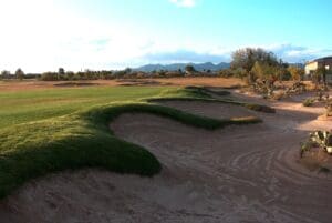 A golf course with sand and grass on the side.